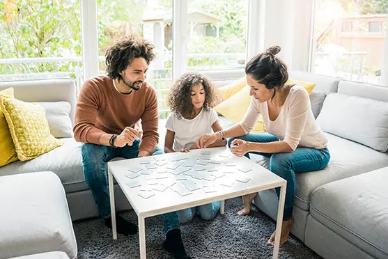 Familie spielt gemeinsam ein Memospiel am Wohnzimmertisch.
